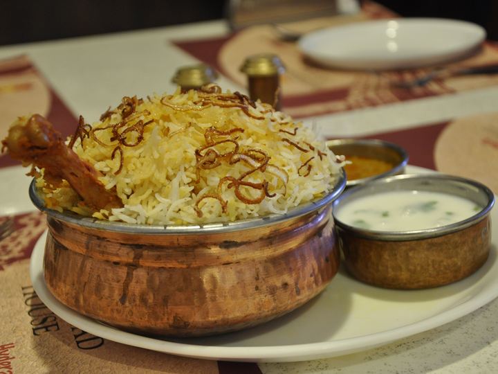 Chicken biryani with saffron-tinted rice and fried onions in a copper bowl with raita