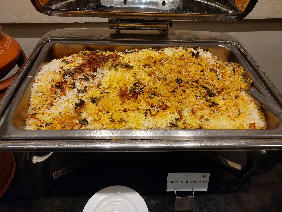 A wide tray of chicken dum biryani with yellow and white rice